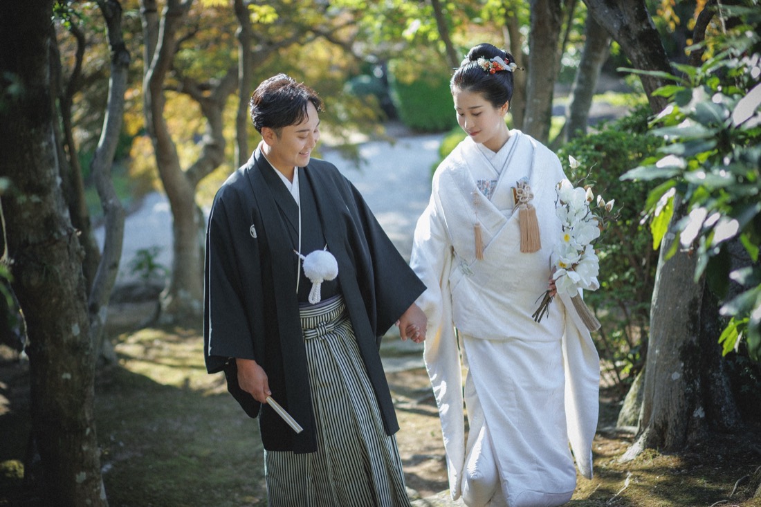 紅葉の庭園を歩む、白無垢と羽織袴姿の新郎新婦。