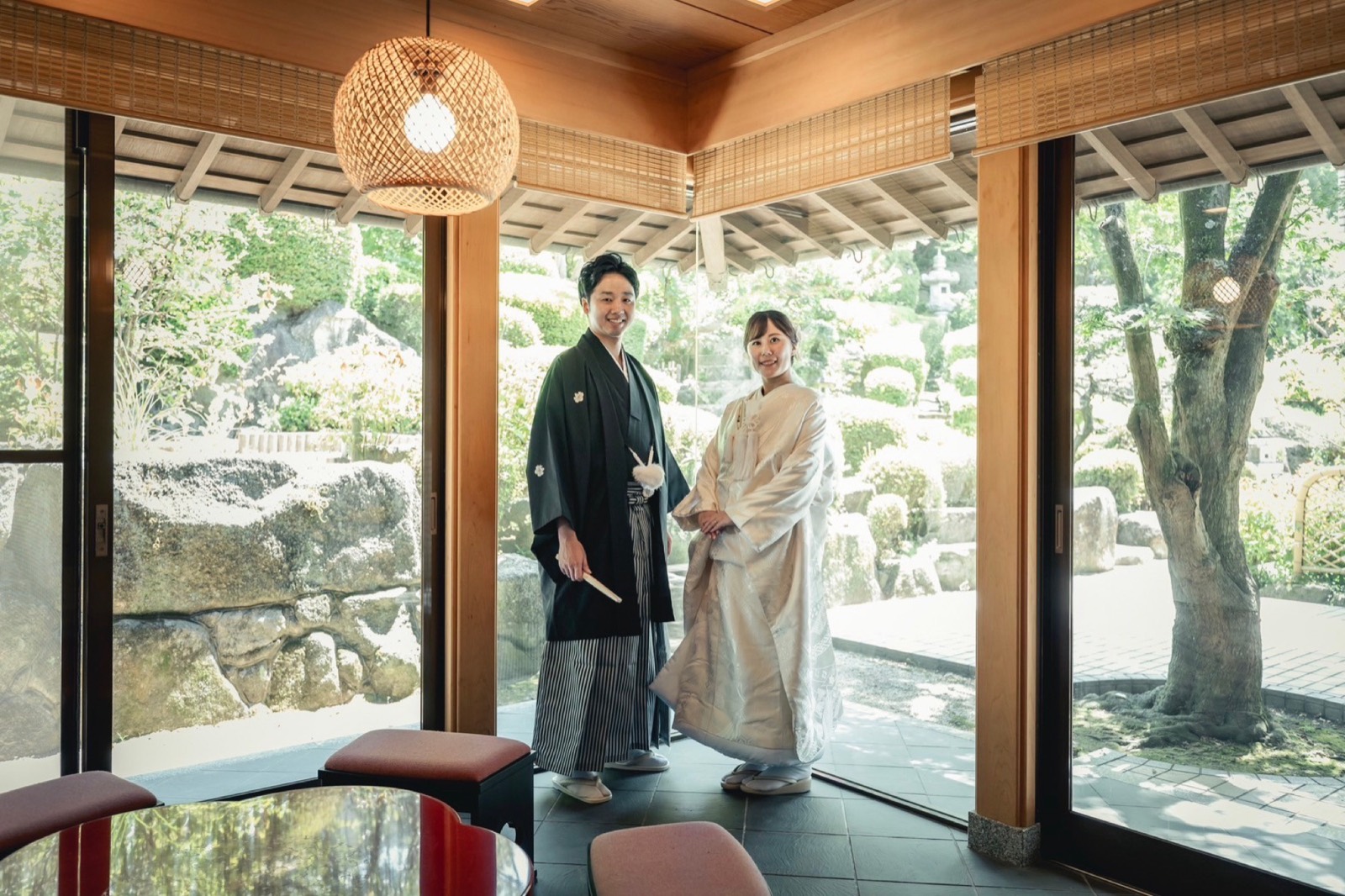 縁側越しに庭園を望む、母屋の室内に立つ新郎新婦。