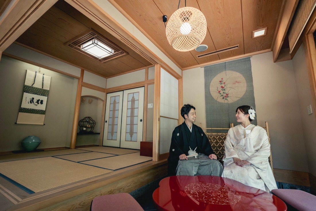 和室の座敷で向き合う新郎新婦。漆塗りの座卓を囲んで。